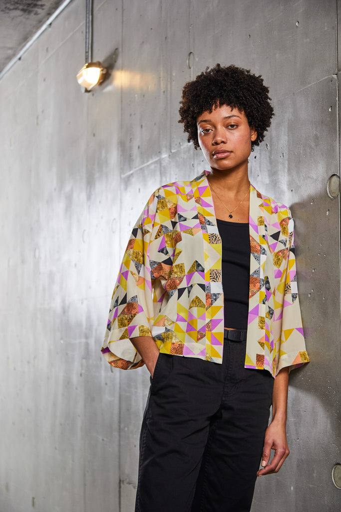 A woman wearing a short silk kimono jacket with geometric triangle print in yellow and pink