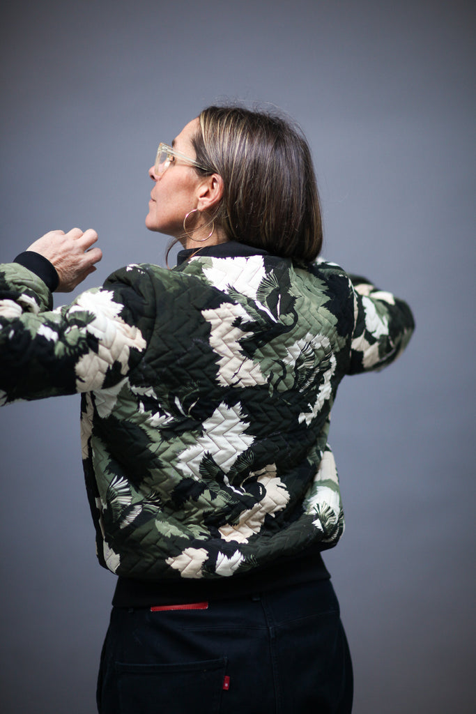 The back of a woman wearing a quilted silk bomber jacket in a green and white camouflaged print 