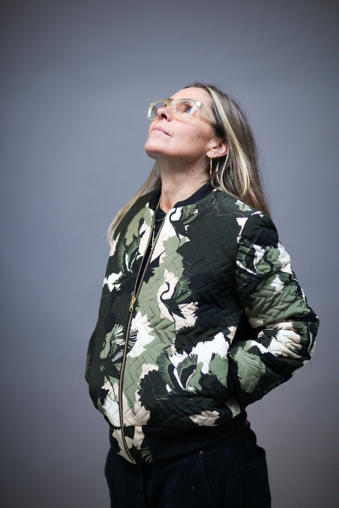 A woman wearing a quilted silk bomber jacket in a green and white camouflaged print 