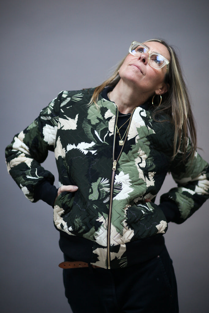 A woman wearing a quilted silk bomber jacket in a green and white camouflaged print 