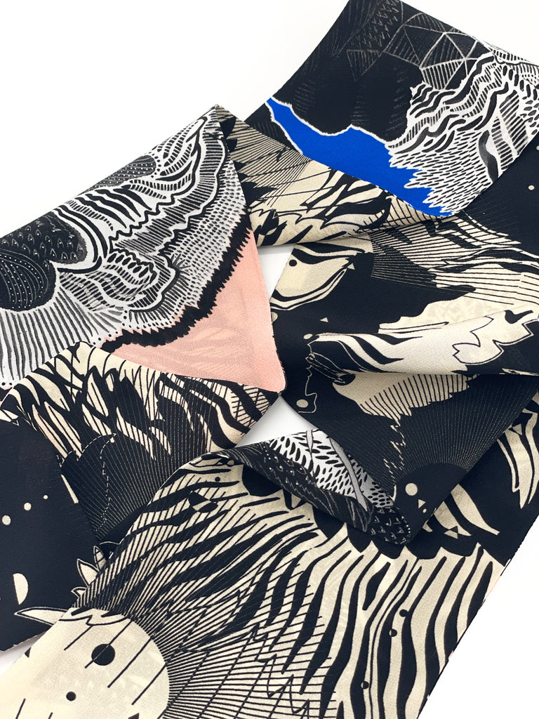 A close up of a silk printed headscarf in black, blue, pink and white
